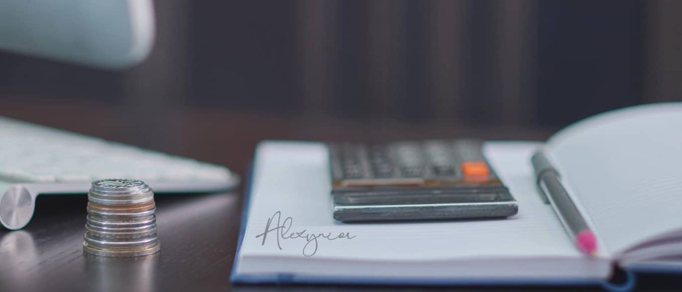 Una pila de monedas junto a un cuaderno abierto con un bolígrafo y una calculadora, sobre un escritorio oscuro. Una firma digital aparece sobre el cuaderno.