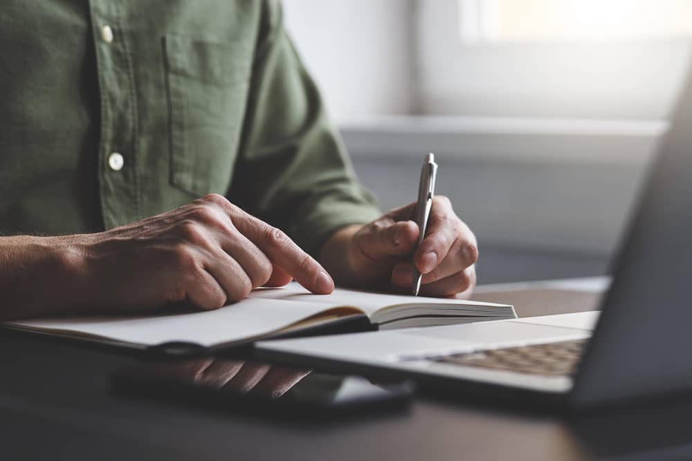 Hombre en su escritorio que planifica tu día escribiendo en una libreta para lograr la máxima productividad.